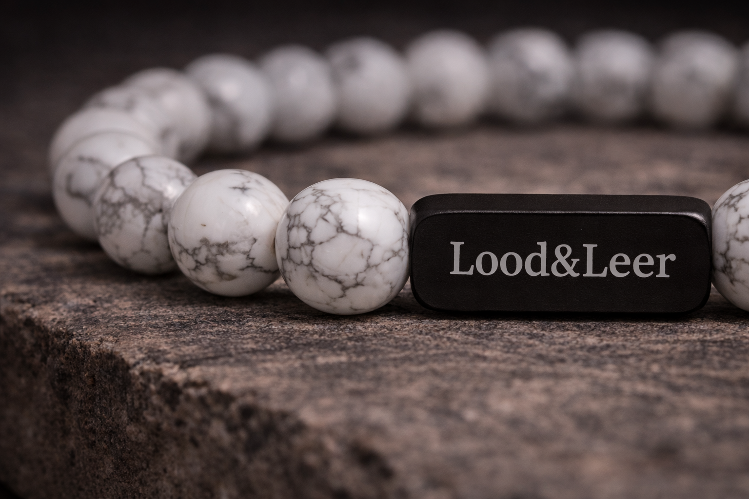 Close-up van een herenarmband van howliet natuursteen met zwarte Lood & Leer stainless steel tag op een robuuste houten ondergrond.