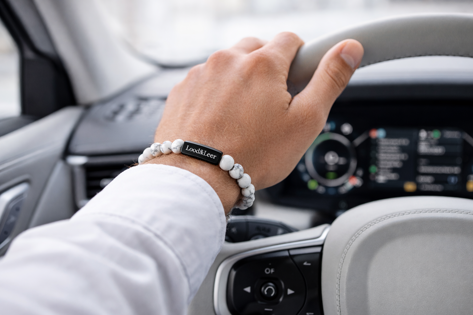 Herenarmband van howliet natuursteen gedragen om de pols tijdens het autorijden, met zwarte Lood & Leer tag.