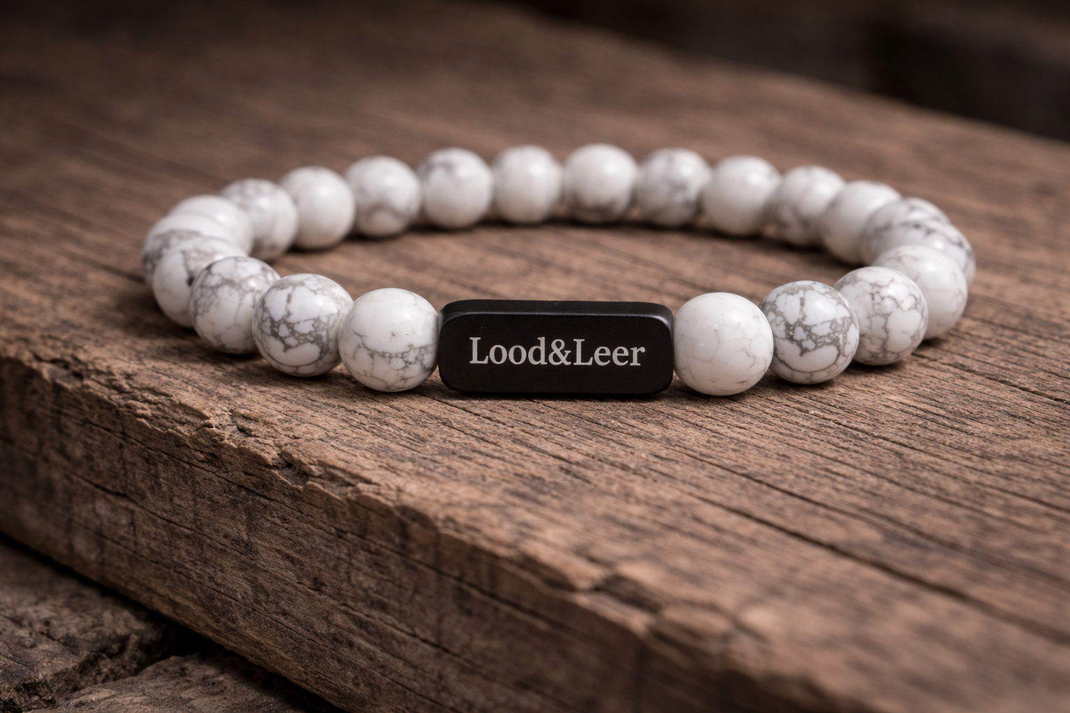 Volledig zicht op een herenarmband van howliet natuursteen met zwarte Lood & Leer tag, gefotografeerd op hout.