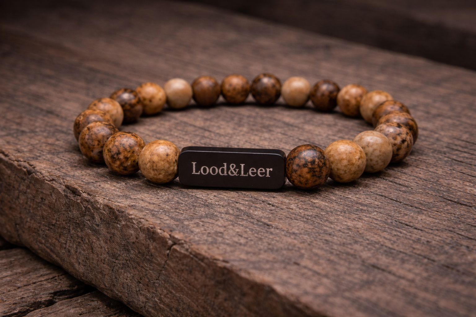 Volledig zicht op een herenarmband van jaspis natuursteen met zwarte Lood & Leer tag, gefotografeerd op hout.