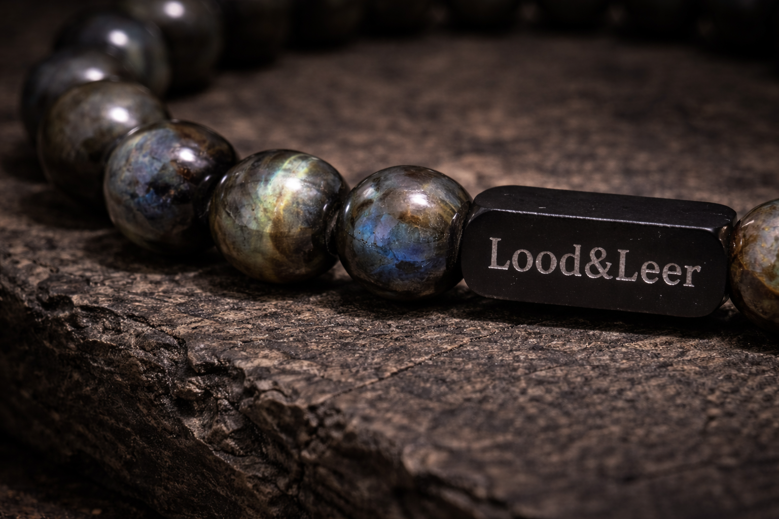 Close-up van een herenarmband van labradoriet natuursteen met zwarte Lood & Leer stainless steel tag op een robuuste houten ondergrond.