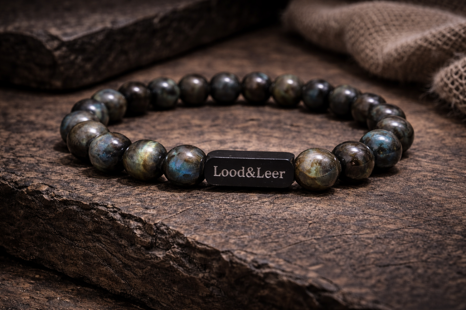 Volledig zicht op een herenarmband van labradoriet natuursteen met zwarte Lood & Leer tag, gefotografeerd op hout.