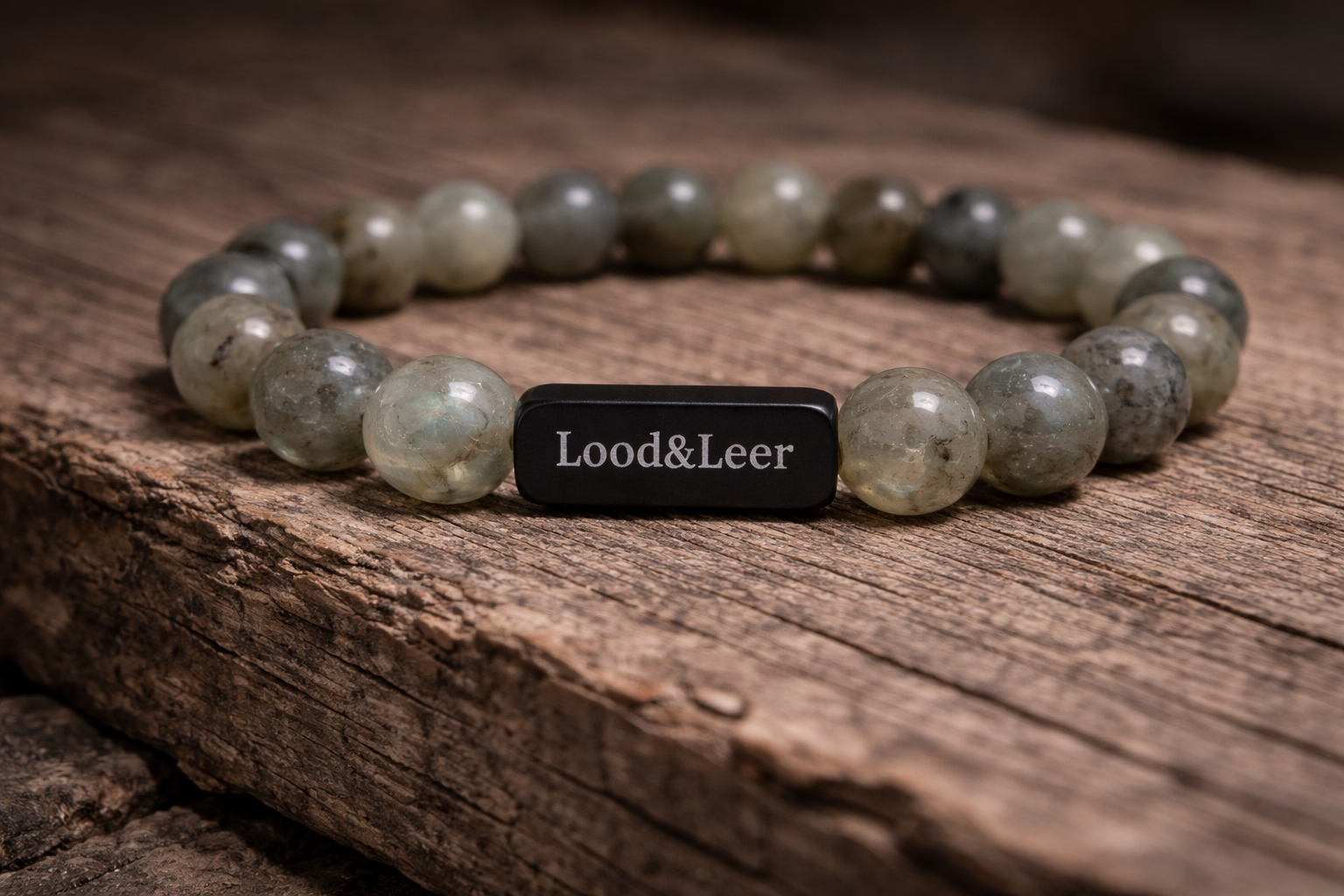 Volledig zicht op een herenarmband van labradoriet natuursteen met zwarte Lood & Leer tag, gefotografeerd op hout.