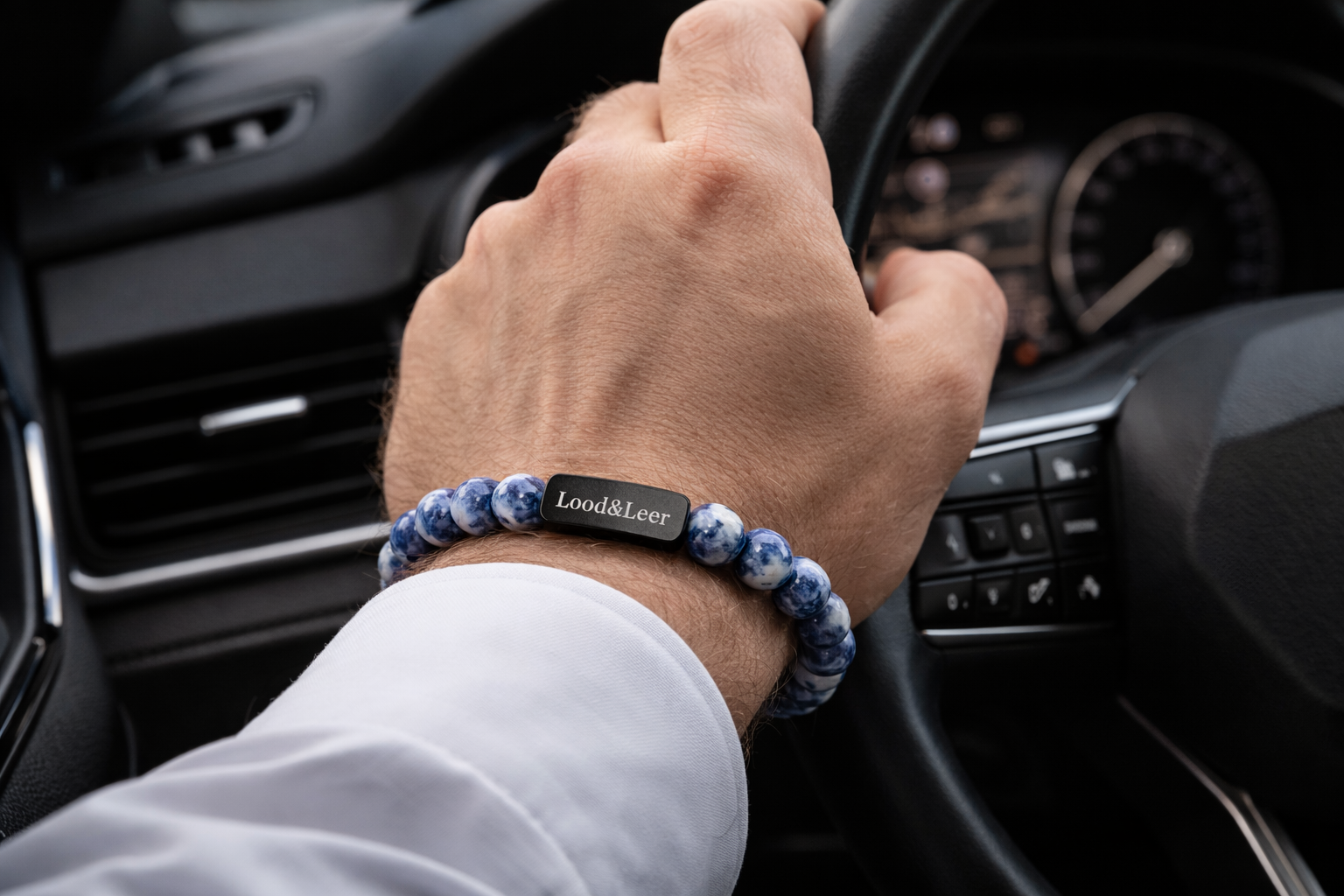 Herenarmband van sodaliet natuursteen gedragen om de pols tijdens het autorijden, met zwarte Lood & Leer stainless steel tag.